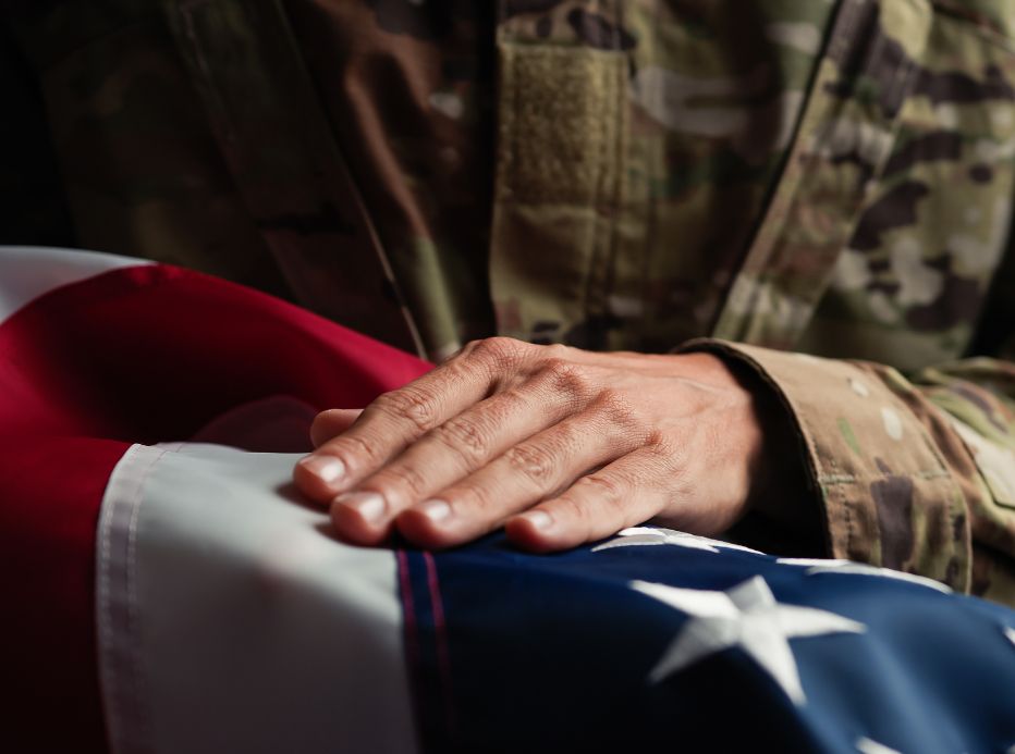 soldier with hand placed on folded US Flag